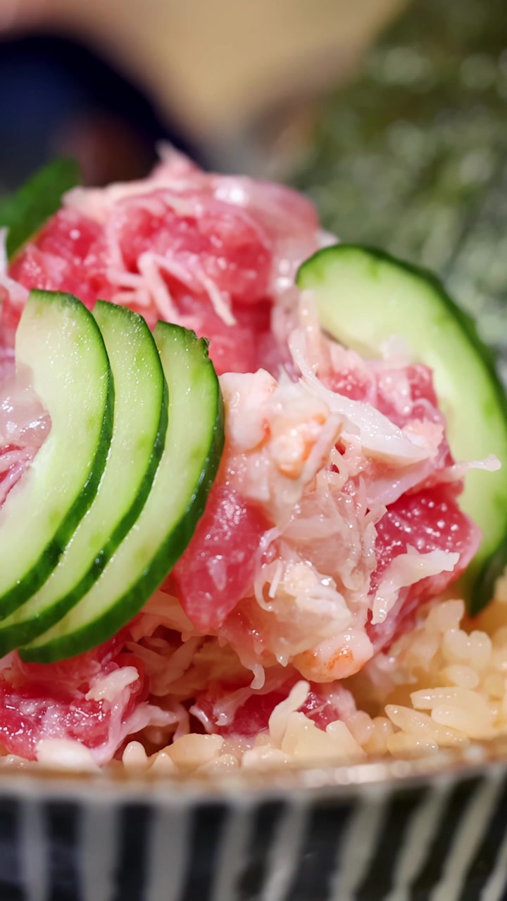 Una cámara en primer plano hace zoom en un tazón de arroz japonés con mariscos, cubierto con cangrejo y atún.
