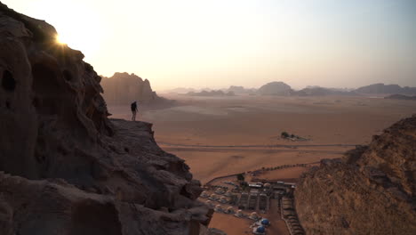 lonely man on rocky hill, viewpoint of vastness of wadi rum desert and bedouin camp, jordan, wide view