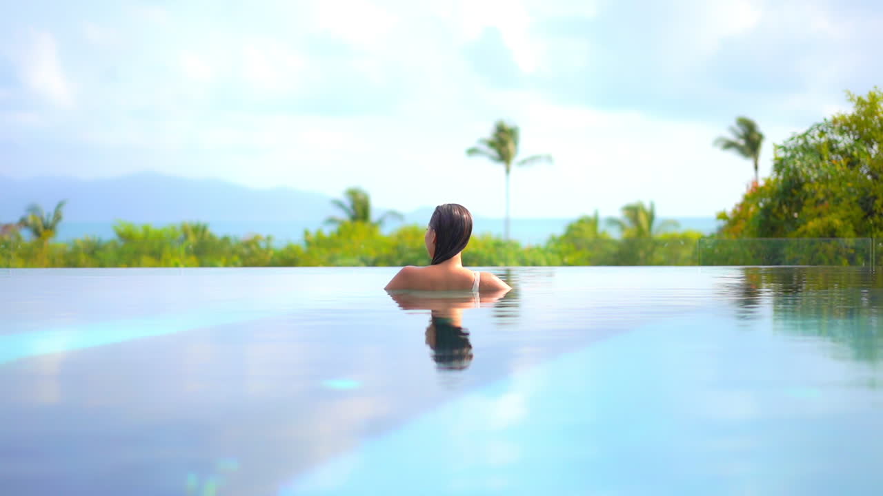 Rückenansicht einer Frau, die im Infinity-Pool entspannt und die Aussicht genießt