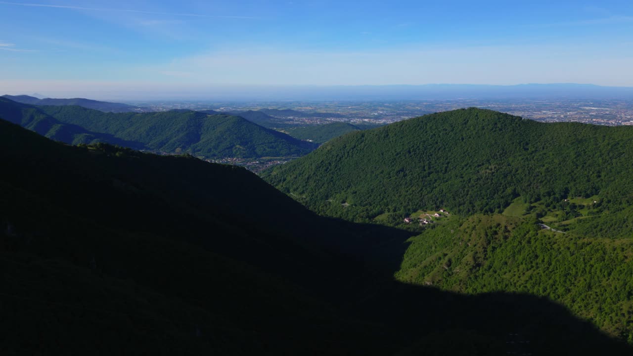 Dramatic aerial view of a steep mountain valley with dark forest shadow and sunlit ridgeline stretching toward flatlands. Shot at Selvino, Italy (Selvino, Italia)