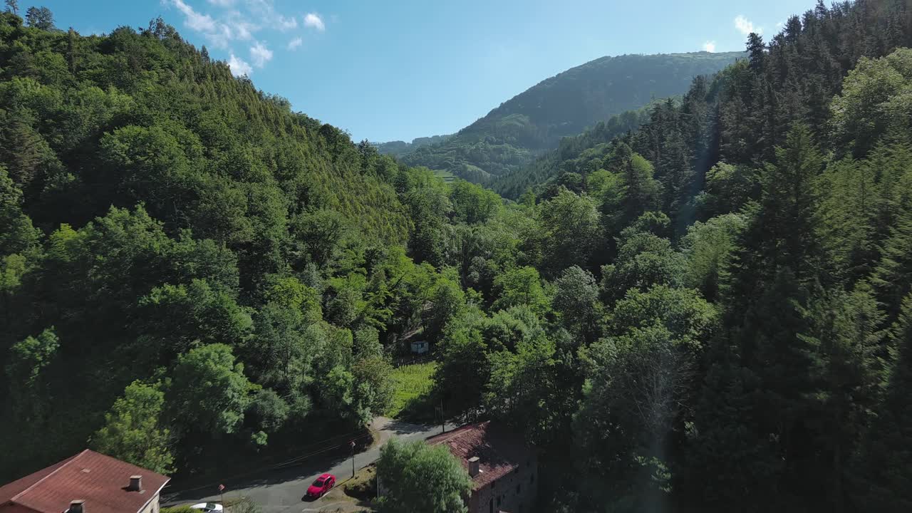 Villaggio dei Paesi Baschi immerso tra lussureggianti montagne verdi sotto cieli blu, vista aerea.