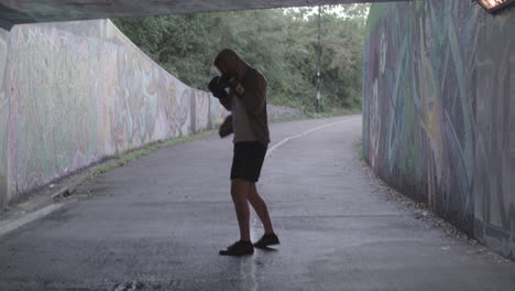 young active man boxing in underpass, silhouetted by light