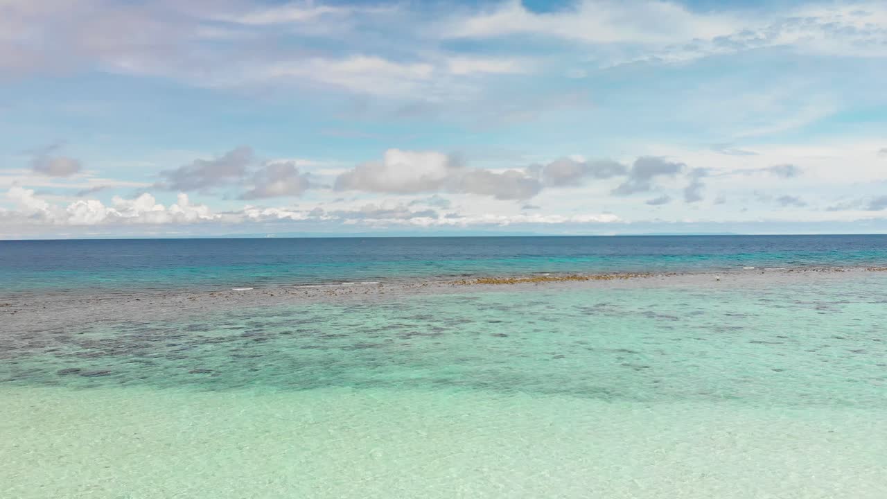 drone flying over shallow bright turquoise tropical ocean showing coral and horizon of sky and clouds