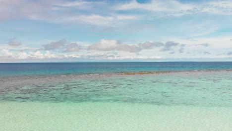 Drone-Volando-Sobre-Un-Océano-Tropical-Turquesa-Brillante-Y-Poco-Profundo-Que-Muestra-Coral-Y-Horizonte-De-Cielo-Y-Nubes