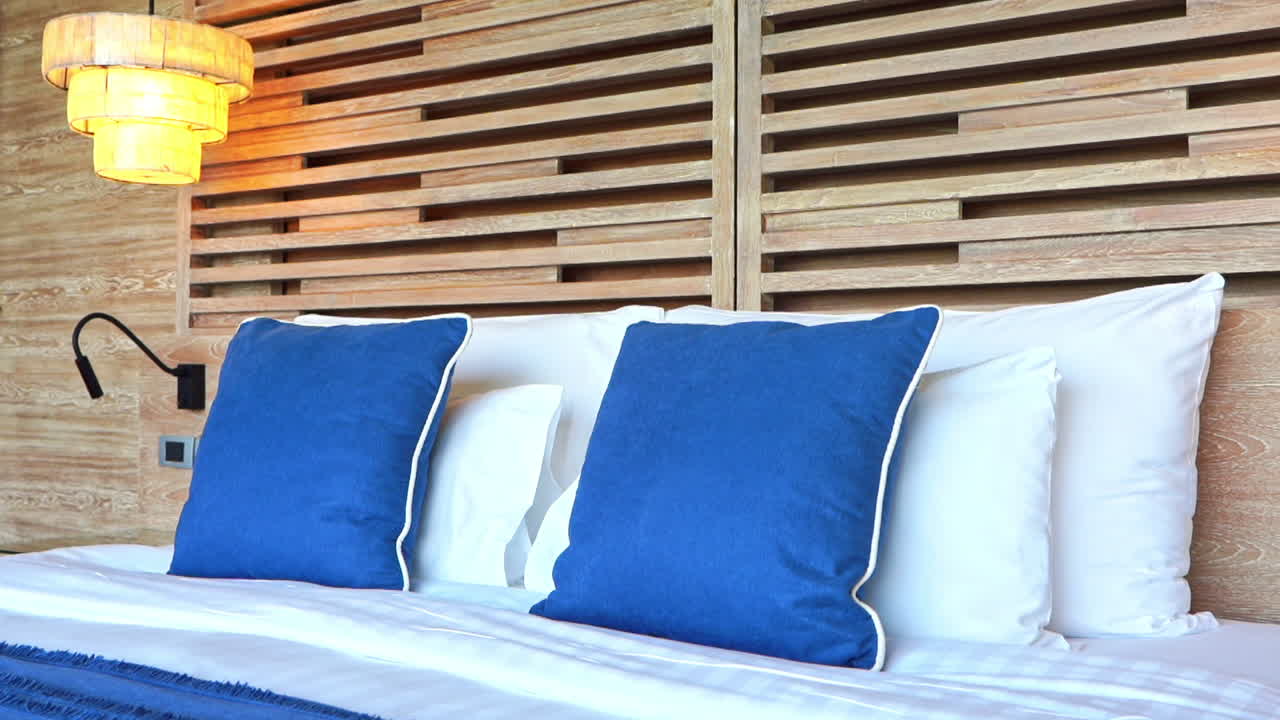 inclinación hacia abajo desde un moderno cabecero de listones de madera hasta una cama de hotel cubierta con almohadas de cama y almohadas y mantas azules decorativas
