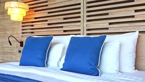 tilt-down from a modern wood slat headboard to a hotel bed covered with bed pillows and decorative blue pillows and blanket