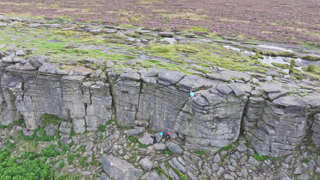los escaladores se sientan en el fondo de la roca de piedra arenisca en el borde de stanage inglaterra, paralaje aéreo