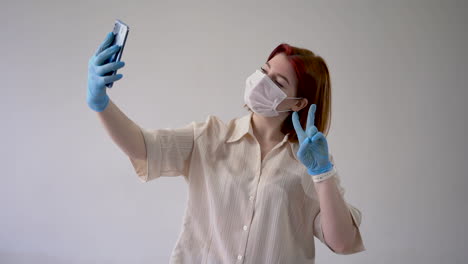 Woman-takes-selfies-wearing-medical-face-mask-and-gloves.-Copy-space-and-white-background.