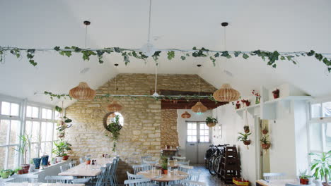 empty tables and chairs in a restaurant dining space in daylight, with feature stone walls and tiled floor, tilt shot