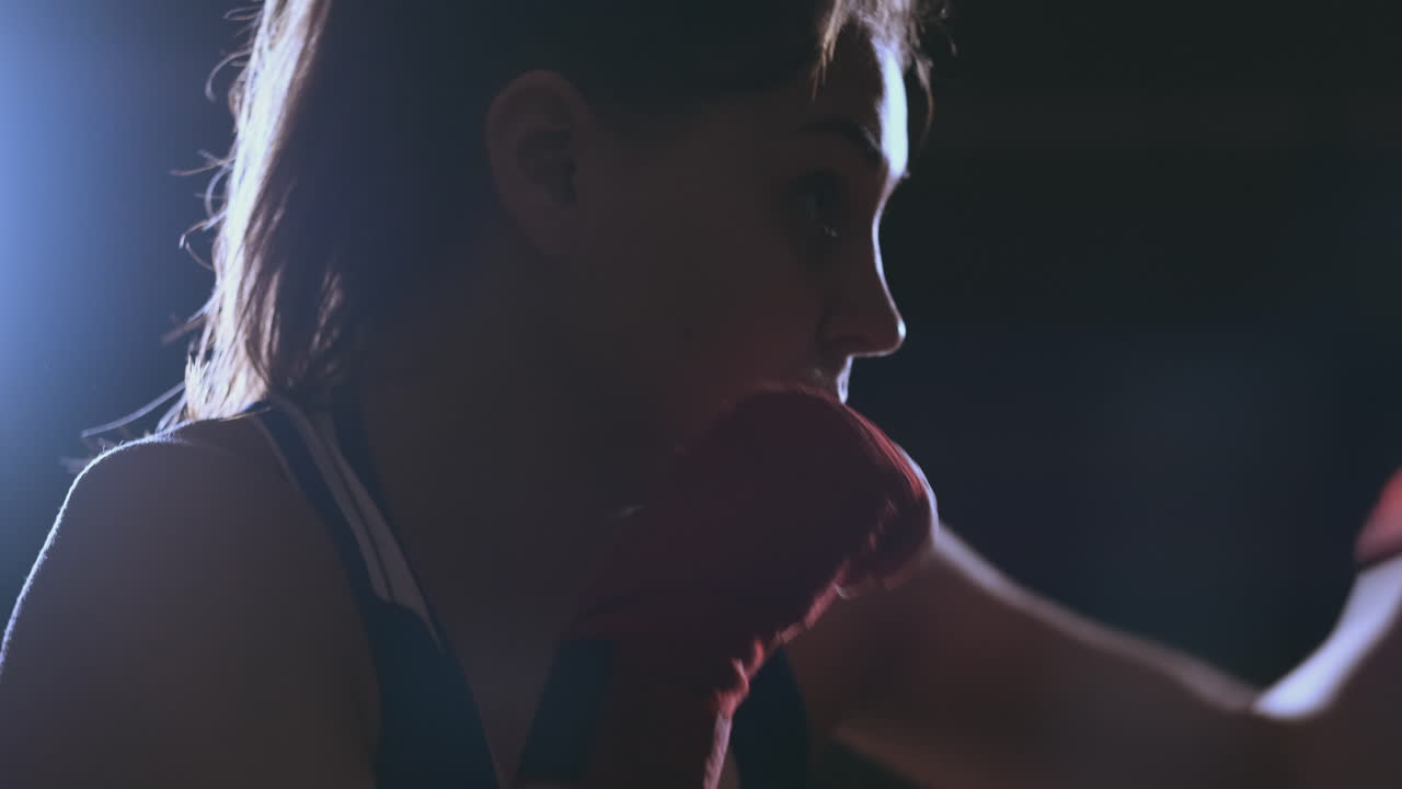 A beautiful woman boxer trains in a dark gym and works out punches in slow motion