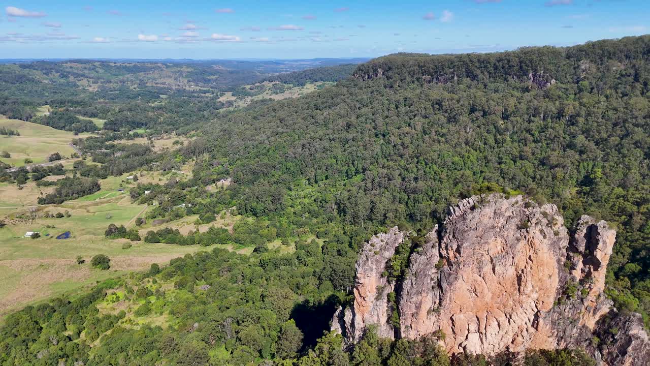 Drone footage captures Nimbin Rocks' rhyolite formations and lush greenery under clear skies, showcasing the area's natural beauty
