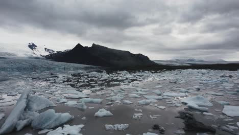 Drone-Volando-En-Círculo-Sobre-Un-Lago-Glaciar-Con-Trozos-De-Hielo-Con-Un-Gran-Glaciar-En-El-Fondo-En-Islandia-4k