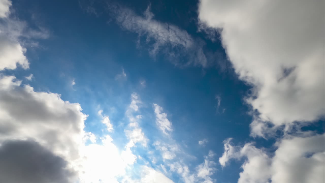 White cotton clouds quickly flying in the sky. Heavy clouds at the backdrop of blue and sunny skies. View from below.