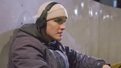 young adult in hoodie wearing headphones resting back on metallic wall while smoking, showcasing a calm and contemplative expression