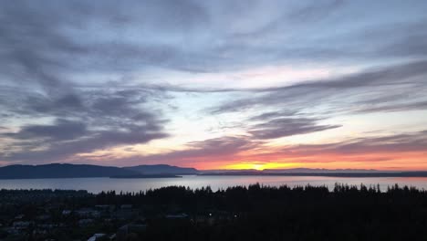 Toma-Aérea-Ascendente-De-Una-Bonita-Puesta-De-Sol-Sobre-Las-Islas-De-San-Juan-Con-Los-Bosques-De-Bellingham-En-Primer-Plano