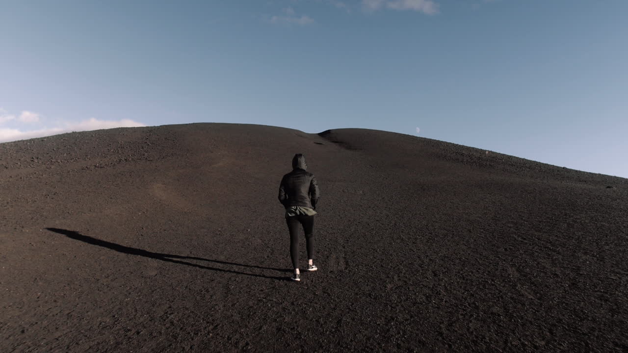 Ampia ripresa con gimbal di una giovane donna minuta che cammina in salita ai Craters of the Moon in Idaho