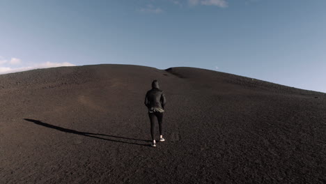 Wide-gimbal-shot-of-young-petite-woman-walking-up-hill-at-craters-of-the-moon-in-Idaho