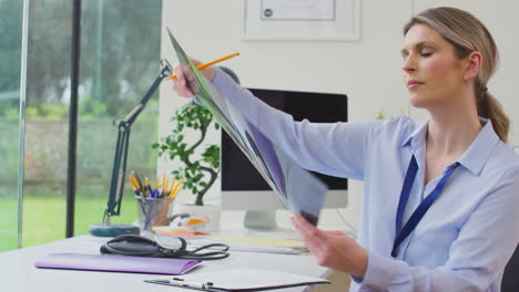 mujer médico o médico de cabecera sentada en el escritorio en la oficina mirando la tomografía computarizada o resonancia magnética
