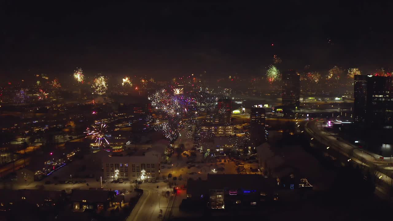New Year's Eve Fireworks Exploding Over Icelandic Cityscape On Winter Night. aerial panning shot