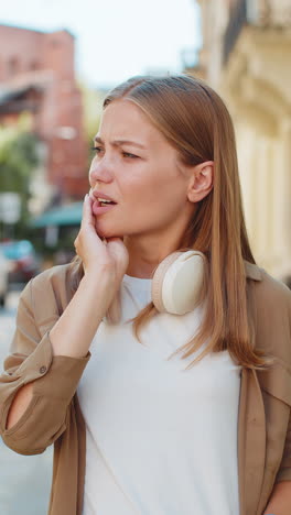 Portrait-of-young-Caucasian-woman-traveler-standing-outdoors-feeling-toothache-on-city-street