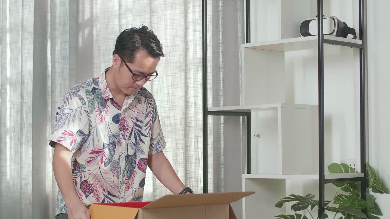 アジア人男性が新しい家に引っ越し紙箱から物を取り出し生息地の本棚を装飾します