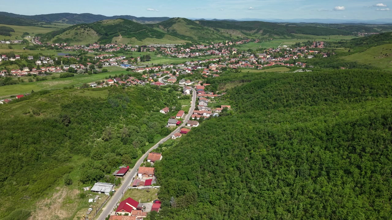 Una prospettiva aerea mostra un piccolo villaggio esteso su una valle verdeggiante con dolci colline.