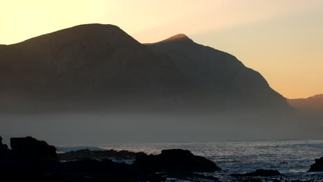 early morning blue hour sun rays over mountain silhouette on hermanus coastline