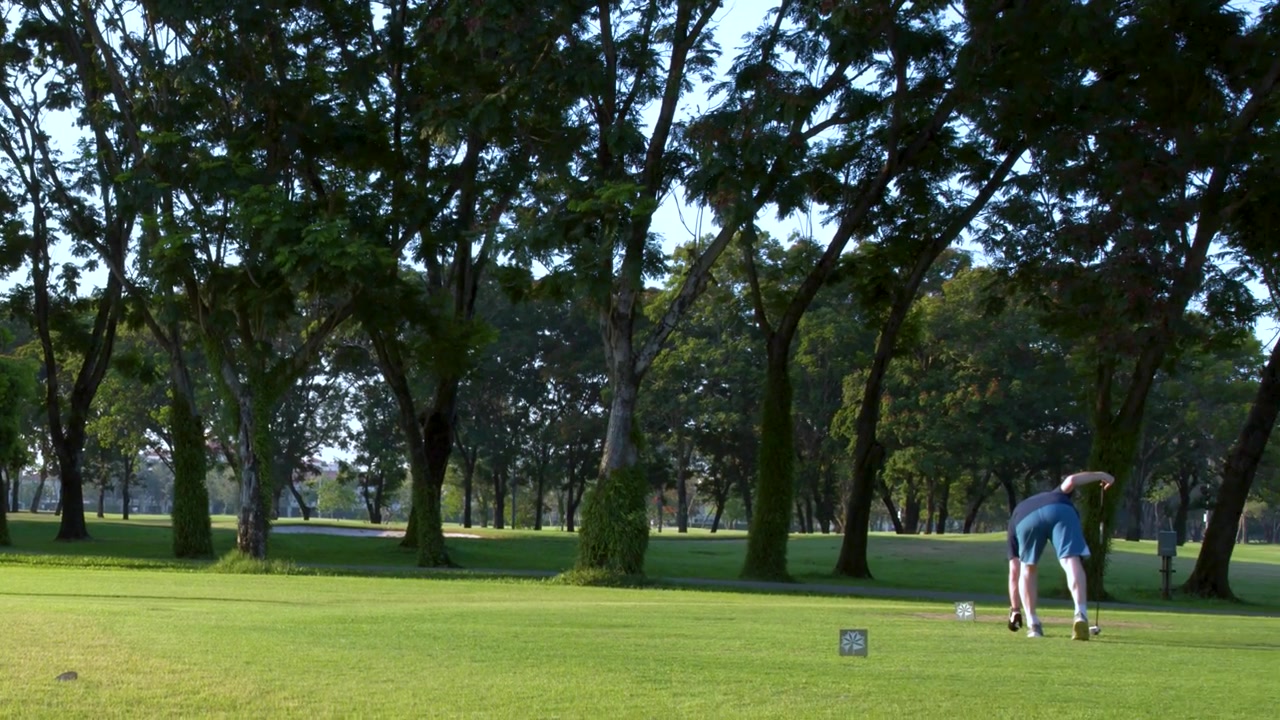 A wide shot pans across a lush golf course as a man prepares his shot.