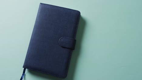 Close-up-of-closed-blue-notebook-with-copy-space-on-green-background-in-slow-motion