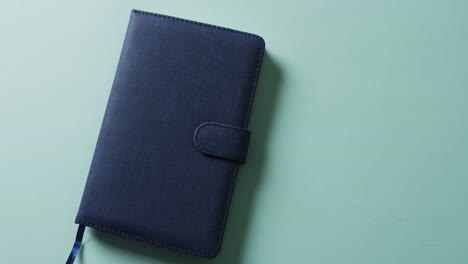 close up of closed blue notebook with copy space on green background in slow motion