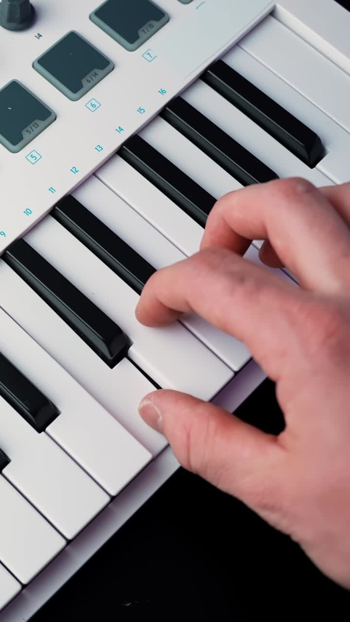 Close-up of a hand playing a melody on a MIDI keyboard controller with soft light and shallow depth of field, ideal for music production b-roll