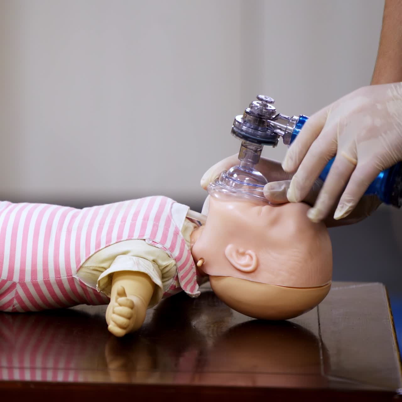 Demonstration of cpr on a baby model. Instructor in medical gloves showing the right breathing exercise on a dummy in training center. Side view