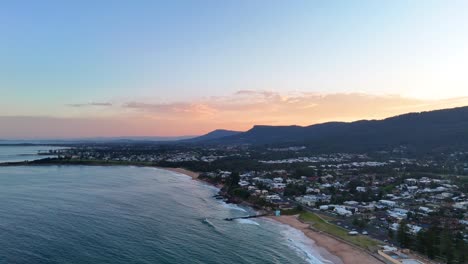 aerial pan of thirroul's coastline at sunset, featuring a tranquil ocean and the warm yellow hues cast across the sky and water