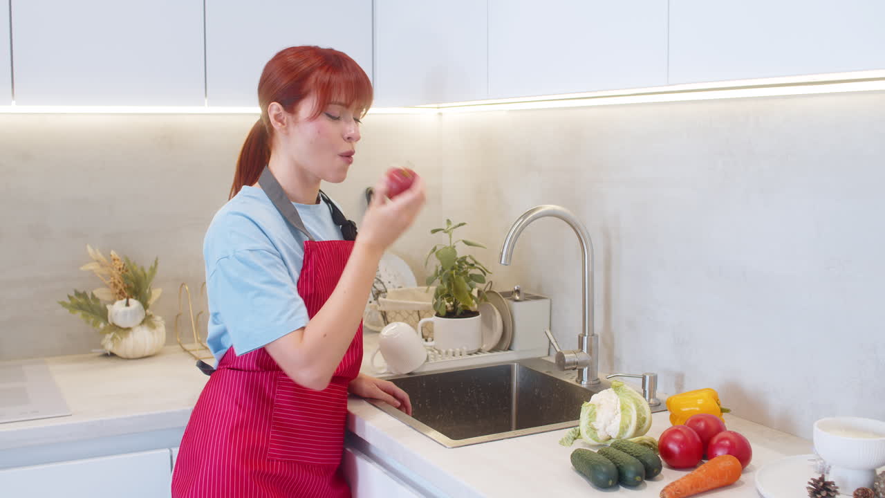 Young woman rinses apple under tap then takes crisp bite clean snack at kitchen sink soft smile calm