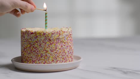 Studio-Shot-Birthday-Cake-Covered-With-Decorations-And-Single-Candle-Being-Lit