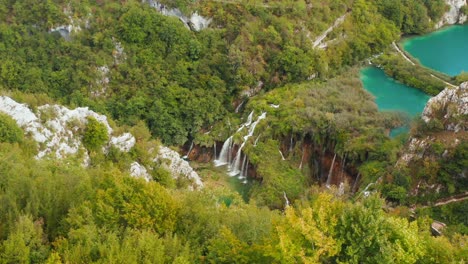 Incredible-aerial-drone-view-of-bright-turquoise-lakes-connected-with-waterfalls-between-rocky-cliffs-and-dense-forest