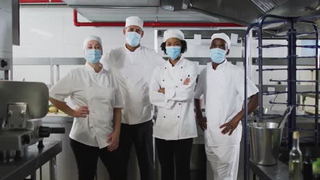 retrato de un grupo diverso de chefs con máscaras faciales de pie en la cocina del restaurante