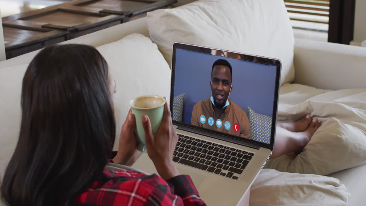 Biracial woman on laptop video chat having coffee at home
