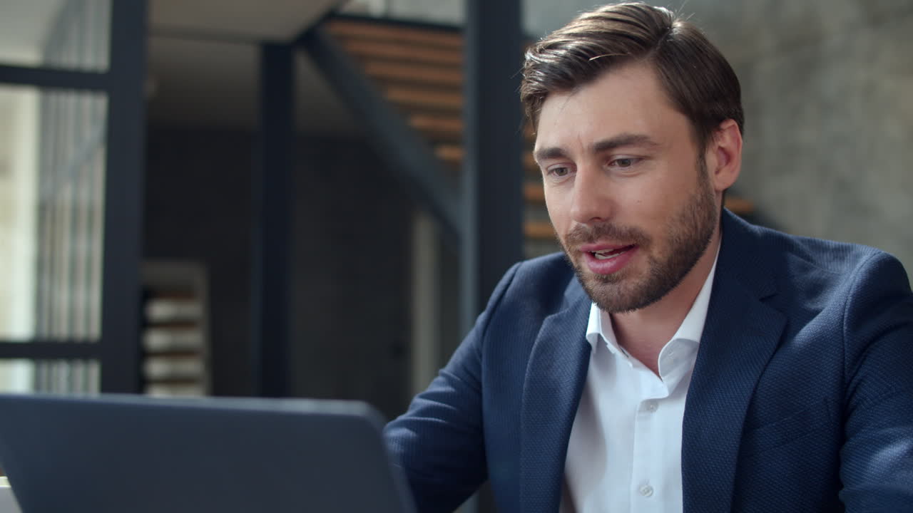 Smiling businessman working with laptop computer and papers in office.