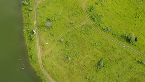 aerial footage revealing vehicles parked at the edge of a river as they are fishing, dirt roads, grass, land features, muak klek, saraburi, thailand