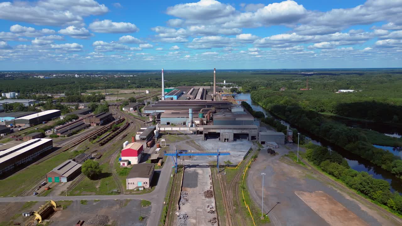 Hennigsdorf electric steel factory with train tracks, chimneys, and industrial buildings under a blue sky. Great aerial view flight overflight flyover drone