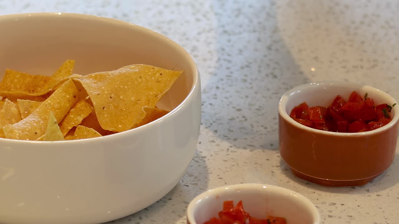 las manos añadiendo salsa a los nachos en un cuenco