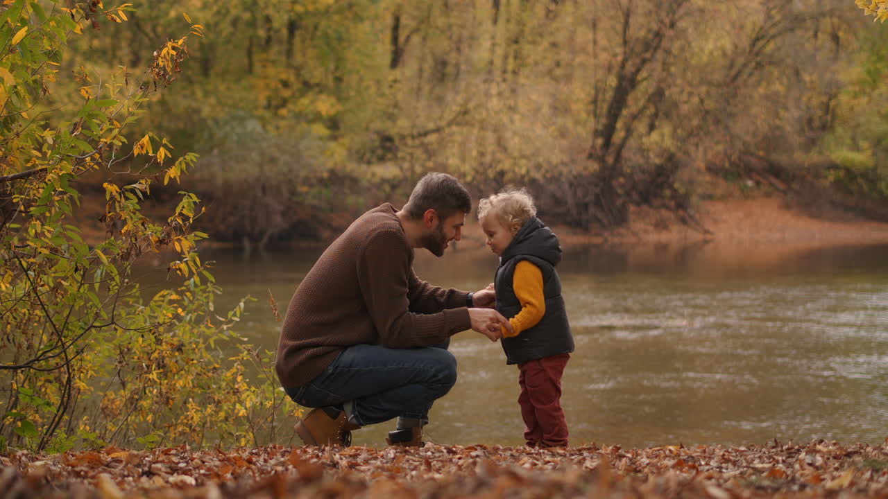 el amoroso padre y el pequeño hijo se comunican en la naturaleza en la orilla del lago en un día de otoño el hombre y el niño se acurrucan por las frentes momentos conmovedores y recuerdos alegres