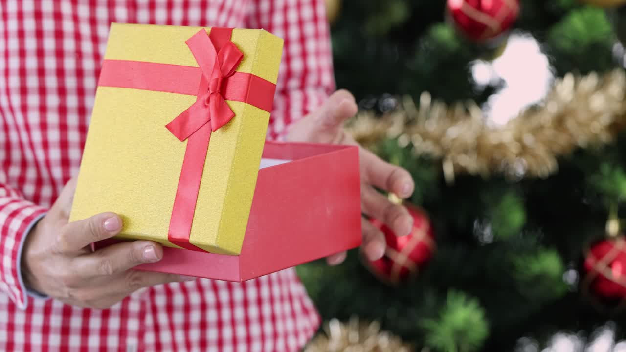 Uomo apre una scatola regalo colorata in piedi vicino all'albero di Natale