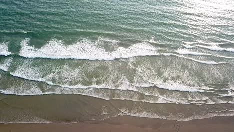 aerial top-down view of ocean waves crashing on sandy beach