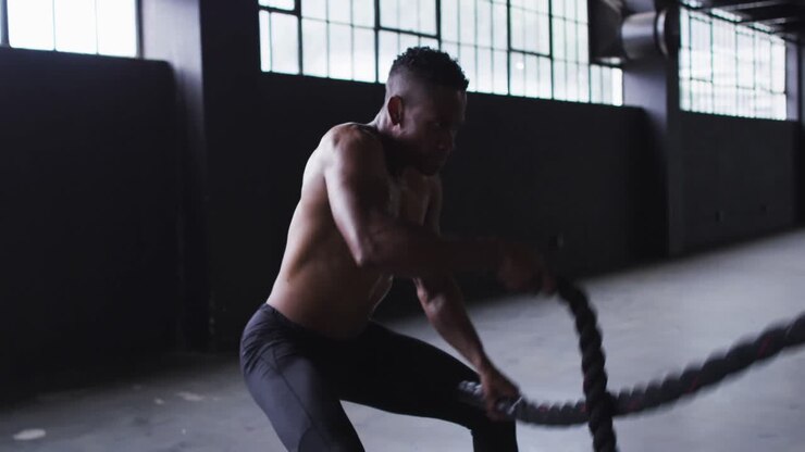 Shirtless african american man exercising battling ropes in an empty urban building