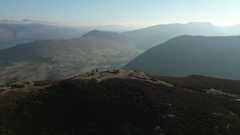 hikers on mountain summit with pull back reveal of green valley and panoramic view of misty mountains beyond in english lake district uk