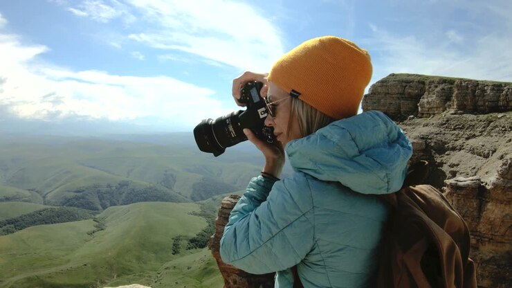 Blonde girl photographer in the cap takes a photo on her digital camera with a background of rocks in the Caucasus