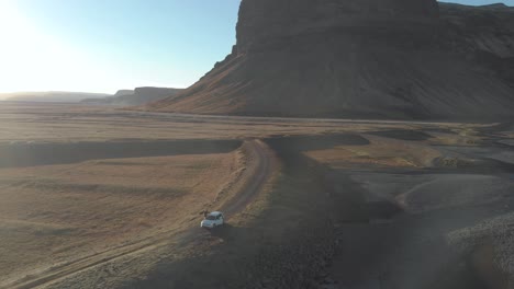 una toma de órbita aérea de un turista saliendo de un coche estacionado en un vasto paisaje
