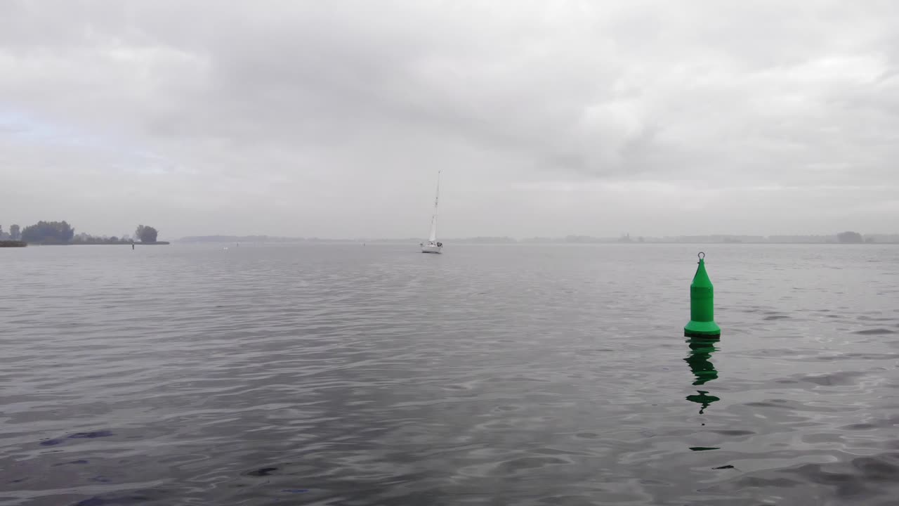 навигационный буй, покачивающийся на спокойном озере, в то время как парусное судно приближается к нему